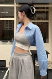 Person wearing a light blue shirt over a gray crop top and pants in front of a store.