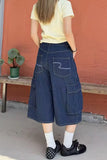 Person wearing blue patterned pants with a yellow shirt and black shoes, standing against a red wall.