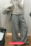 Person wearing a light gray quilted jacket and floral pajama pants, holding a gray blanket.