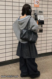Person standing in front of a payphone wearing a gray hoodie, black bag, and plaid skirt.