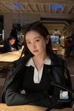 Woman in a black coat and white shirt standing in a modern indoor setting with people in the background.