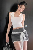 Woman wearing a white top and gray skirt with lace details against a dark background