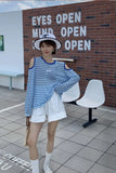 Person wearing a blue striped shirt and white shorts standing in front of a brick wall with motivational text.