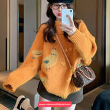 Person wearing an orange sweater with bird patterns, holding a phone and a small handbag.