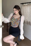 Woman in a floral top and black skirt with sheer white sleeves indoors.