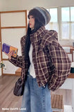 Person wearing a plaid jacket and beanie indoors, holding a product.
