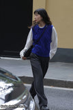 Woman walking on a street wearing a blue knitted vest and carrying a black bag.