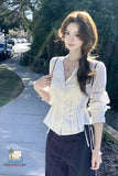 Woman in a white blouse and dark pants standing outdoors on a sidewalk.