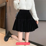 Person wearing a black velvet skirt and white sweater indoors.