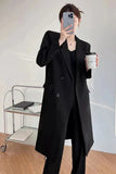 Person wearing a black suit holding a coffee cup in a minimalistic room.