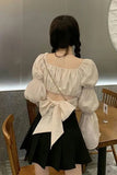 Person wearing a white blouse with puffed sleeves and a black skirt in an indoor setting.