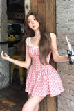 Woman in a pink dress holding a bottle in an indoor setting with a stone wall and wooden door.