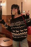 Person wearing a black and white patterned sweater, holding a cup, and making a peace sign indoors.