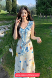 Woman in a floral dress standing in a scenic outdoor setting with mountains and trees.