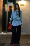 Person wearing a light blue shirt and dark pants, holding a red bag, standing in front of a door.