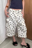 Person wearing a navy polka dot top and white pants with black polka dots, standing indoors.