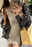 Person wearing a gray dress with a black and white striped cardigan, holding a phone and a shopping bag.