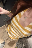 Person wearing a yellow and white striped top with a necklace, standing in a kitchen.