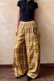 Person wearing yellow plaid pants and a black top against a beige wall.