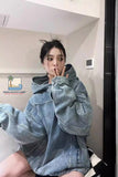 Person wearing an oversized denim jacket in a room with a visible brand logo.