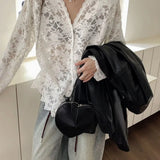 Person wearing a white lace top and holding a black handbag indoors.