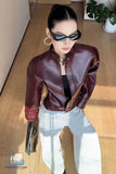 Woman wearing a brown leather jacket and sunglasses indoors.