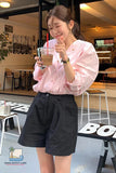Woman in a pink shirt and black shorts holding a drink with a straw in an indoor setting.