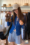 Woman in a clothing store holding a teddy bear, wearing a blue cardigan and gray cap.
