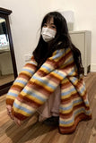Person wearing a colorful striped blanket over their shoulders in an indoor setting.