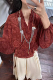 Person wearing a red patterned blouse with long necklaces indoors.