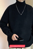 Person wearing a black turtleneck sweater holding a phone against a neutral background