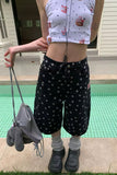 Person wearing a white sleeveless top with pink designs and black polka dot pants, standing by a pool.