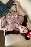 Person wearing a plaid dress with a red bow, lying on a beige couch.