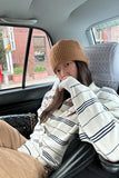 Person sitting in a car wearing a beige beanie and striped sweater.