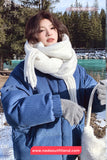 Person wearing a blue coat and white scarf in a snowy landscape with trees and water.