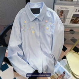 Blue and white striped shirt with floral embroidery on a chair with magazines in the background.