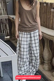 Person wearing a brown tank top and plaid pants standing on a patio.