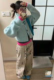 Person taking a mirror selfie wearing a light blue cardigan, pink sweater, floral pants, and blue shoes.