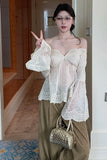 Woman wearing a white lace top and green pants, holding a handbag indoors.