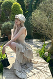 Woman in a beige dress and hat sitting outdoors in a garden setting