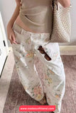 Person wearing floral pants with a beige top and holding a textured handbag.