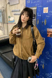 Person wearing a brown jacket holding a drink in front of a blue wall with graphics.