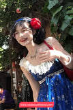 Woman in a blue dress with white lace details and a red flower headband, standing outdoors.