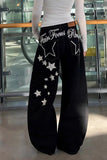Person wearing black pants with star designs and text, standing in a modern indoor setting.