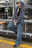 Person wearing a plaid jacket and jeans sitting on a metal railing outside a building.