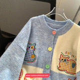 Children's sweater with cat designs and colorful buttons on a hanger.