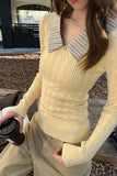 Person wearing a light yellow sweater with a striped collar, holding a coffee cup outdoors.