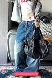 Person wearing a white crop top with a logo, blue jeans, and holding a black handbag in an indoor setting.