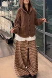 Person wearing a brown knitted hoodie and plaid pants in an indoor setting.