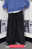 Person wearing a blue sweatshirt and black wide-leg pants standing against a white wall with printed text.